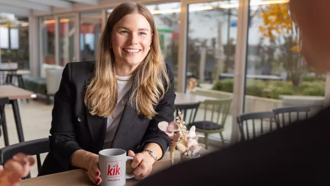 Una giovane collaboratrice con una tazza di caffè durante una pausa insieme ai colleghi nella mensa aziendale