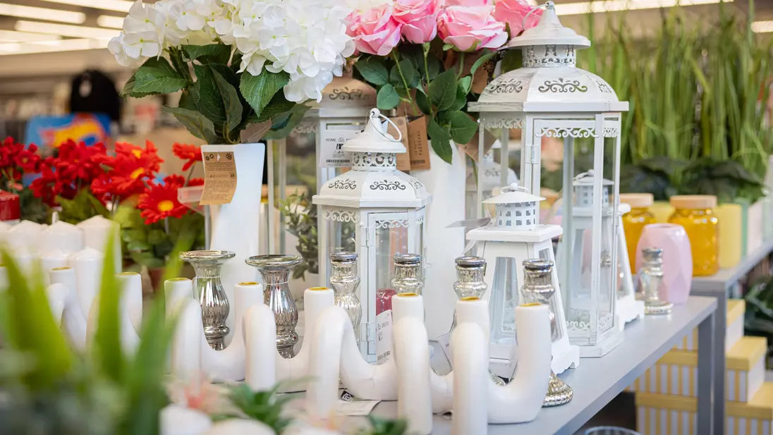 Articoli decorativi e fiori artificiali dell’assortimento non food KiK esposti su un tavolo espositivo a gradoni nell'area d'ingresso del punto vendita