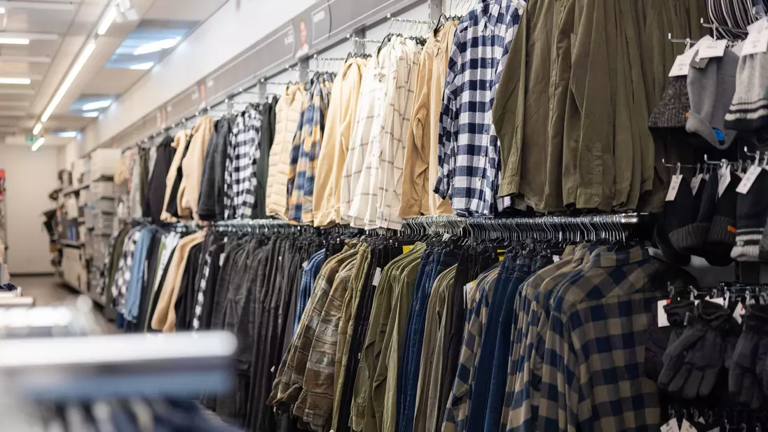 Capi di abbigliamento maschile esposti su appendiabiti lungo la parete di fondo di un punto vendita KiK