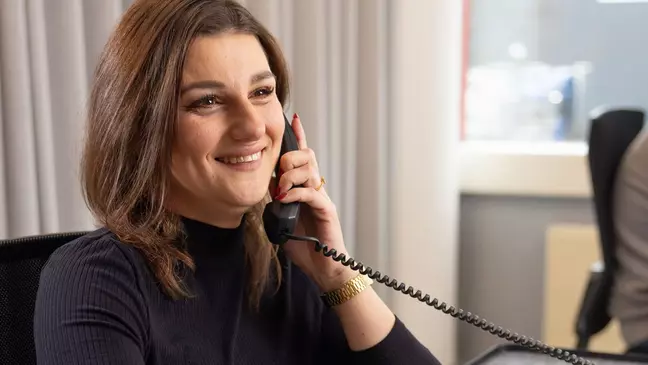 Una donna sorride mentre parla al telefono dalla propria postazione di lavoro
