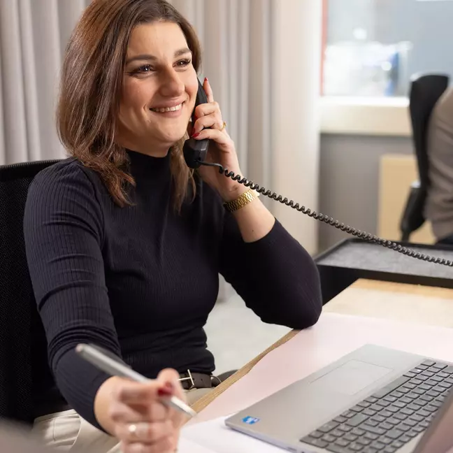 Una donna sorride mentre parla al telefono dalla propria postazione di lavoro