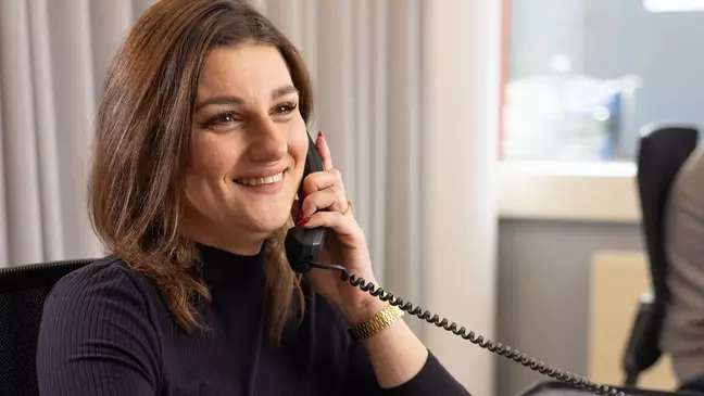 Una donna sorride mentre parla al telefono dalla propria postazione di lavoro