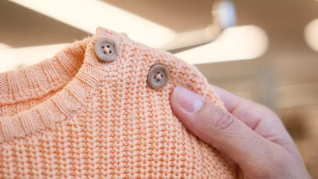 Una mano tiene in mano un maglione arancione da bambino con bottoni sullo scollo