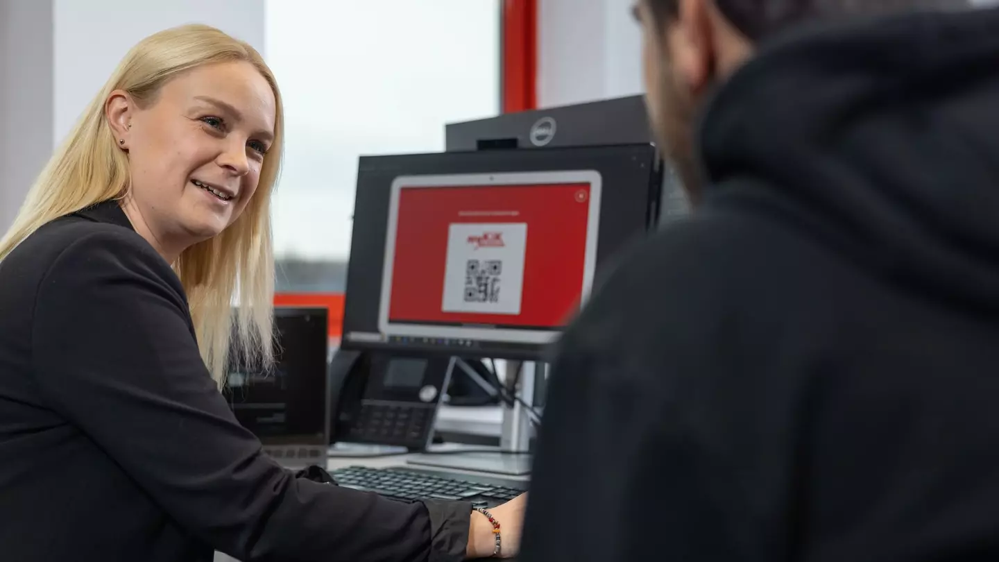 Eine Frau und ein Mann sitzen vor einem Computer, die Frau lächelt und wendet sich dem Mann zu