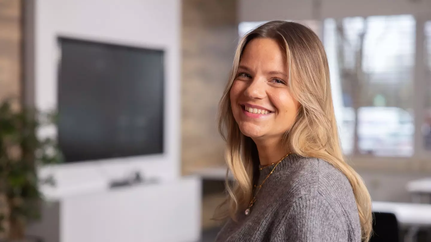 Una donna sorride alla fotocamera all’interno di un ambiente di lavoro moderno